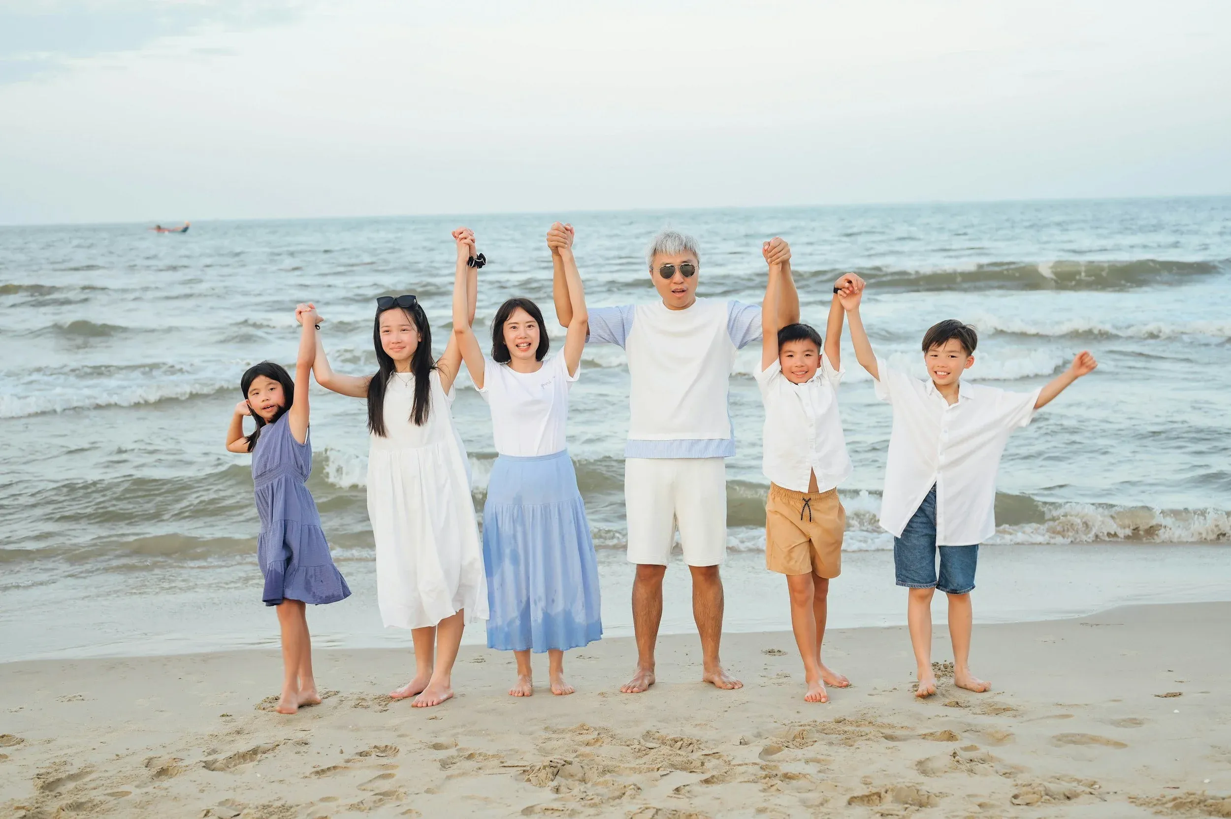 A family of adults and children holding hands on a beach beside the sea