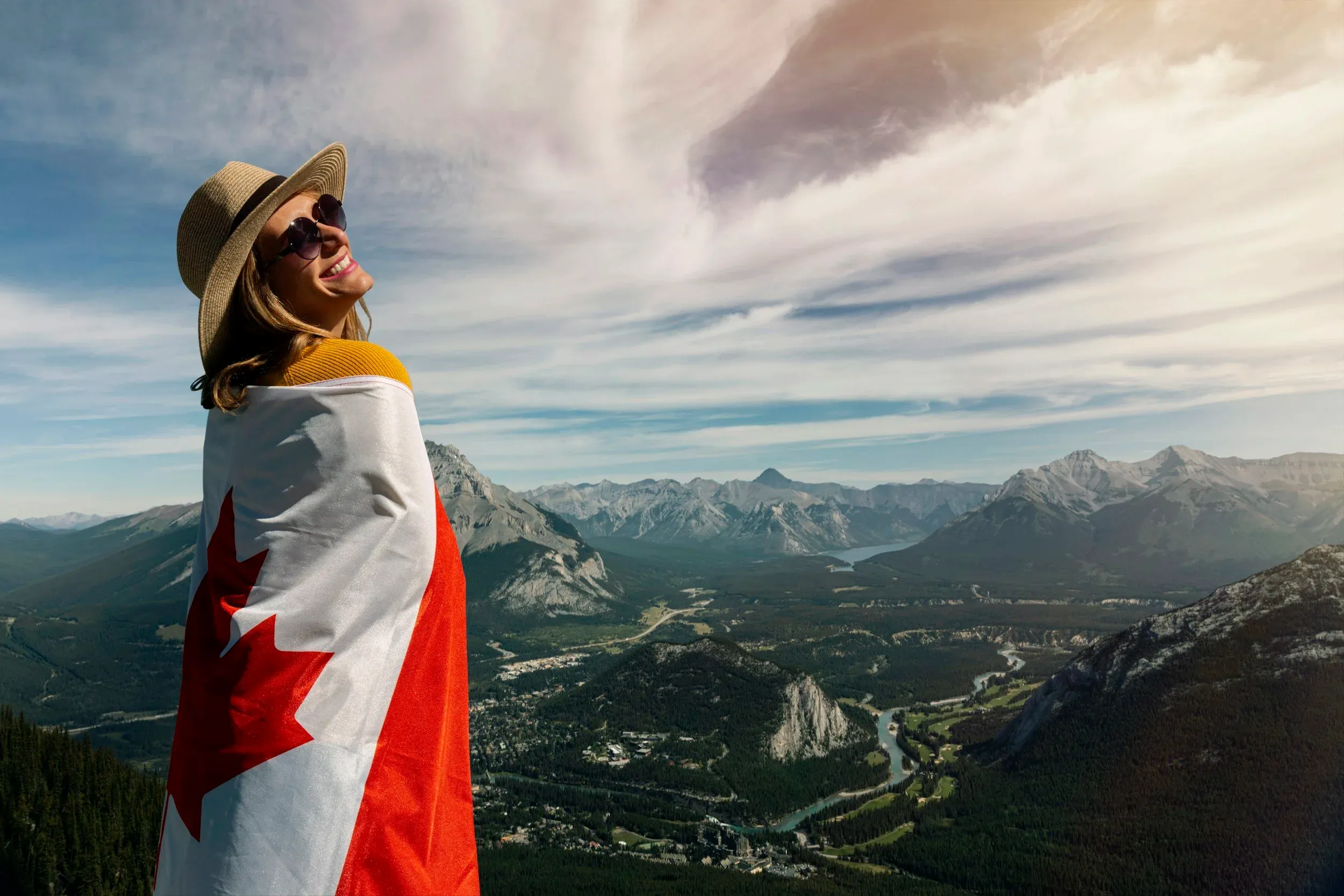 Smiling woman wearing a Canadian flag as a cape above a mountain valley in Canada